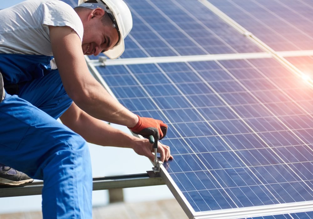 Professional technician installing solar photo voltaic panel to metal platform using screwdriver. Stand-alone solar panel system installation, efficiency and professionalism concept.
